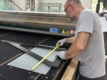 Découpe verre sur mesure : un miroitier MSO contrôle les cotes d’un gabarit dans l’atelier de Lormont